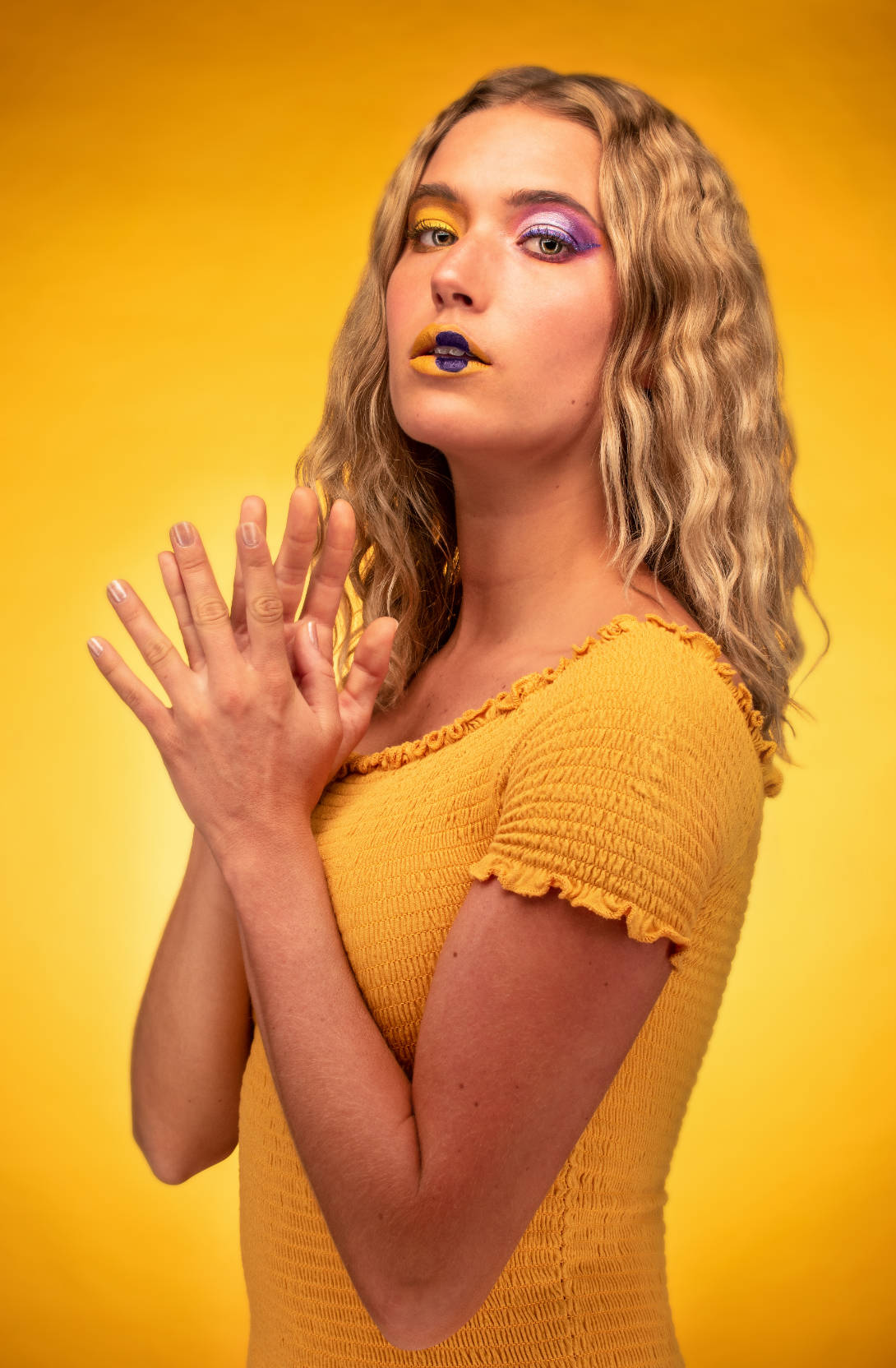 Fotografía plano medio de una joven con maquillaje en tonos amarillos y morados.