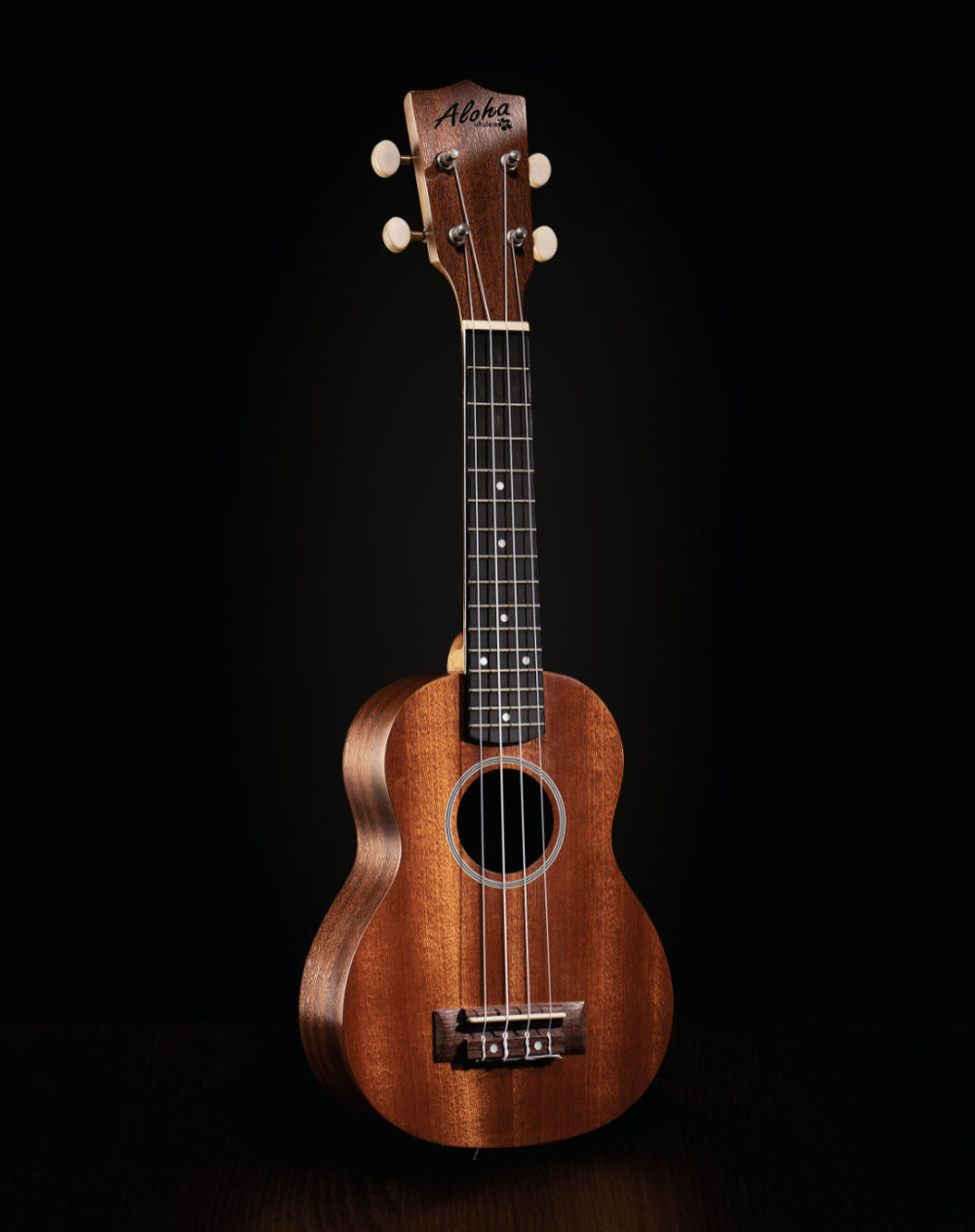Fotografía de ukulele marca Aloha sobre fondo negro.